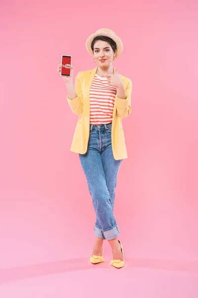 Kyiv, ukraine - 24. April 2019: attraktive Mixed Race Frau zeigt Smartphone mit Youtube App auf dem Bildschirm auf rosa Hintergrund. — Stockfoto