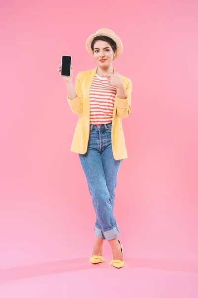 Sonriente mujer de raza mixta mostrando teléfono inteligente con pantalla en blanco sobre fondo rosa - foto de stock