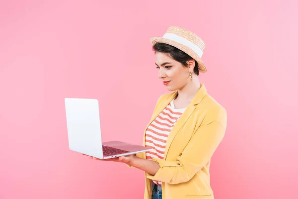 Attrayant mélange race femme en paille chapeau en utilisant ordinateur portable isolé sur rose — Photo de stock
