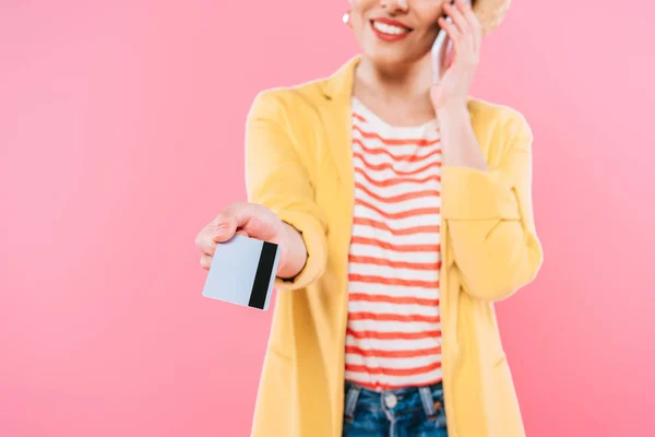 Vista parcial de la mujer de raza mixta hablando en el teléfono inteligente y la celebración de la tarjeta de crédito aislado en rosa - foto de stock