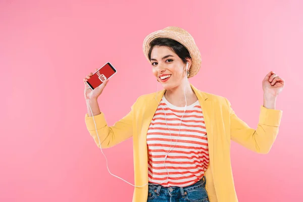 KYIV, UCRAINA - 24 APRILE 2019: Allegra donna mista che tiene smartphone con app Youtube sullo schermo e ascolta musica in auricolare isolata su rosa . — Foto stock
