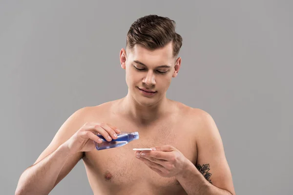 Smiling nude young man applying lotion on cotton pad isolated on grey — Stock Photo