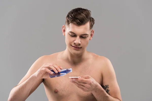 Sourire nu jeune homme appliquant de la lotion sur un coton isolé sur du gris — Photo de stock