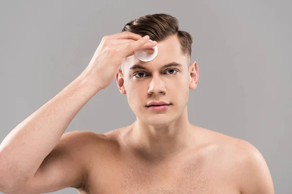 Front view of handsome young man wiping face with cotton pad isolated on grey — Stock Photo