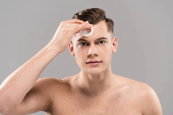 Vue de face du beau jeune homme essuyant visage avec coton isolée sur gris — Photo de stock