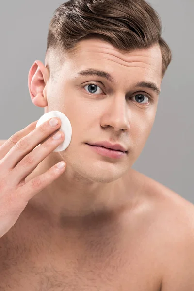 Beau jeune homme essuyant visage avec tampon de coton isolé sur gris — Photo de stock