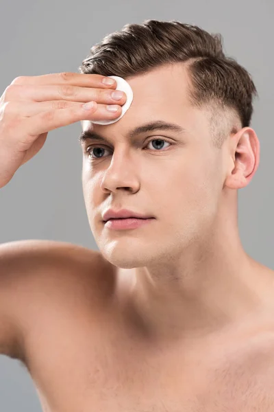 Beau jeune homme essuyant visage avec tampon de coton isolé sur gris — Photo de stock