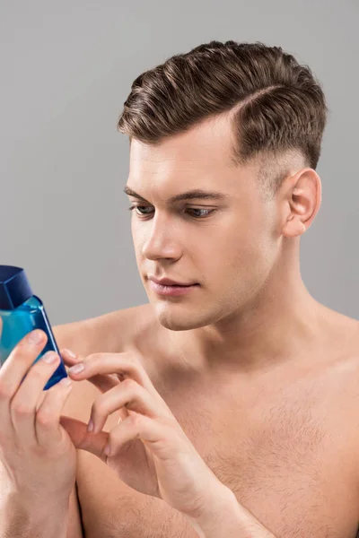Enfocado joven desnudo mirando botella de loción aislado en gris - foto de stock
