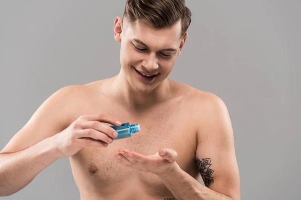Smiling naked young man applying lotion on hand isolated on grey — Stock Photo