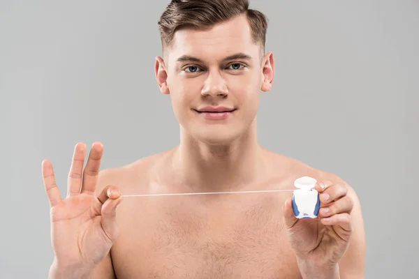 Вид спереду красивий голий молодий чоловік тримає зубну нитку ізольовано на сірому — стокове фото