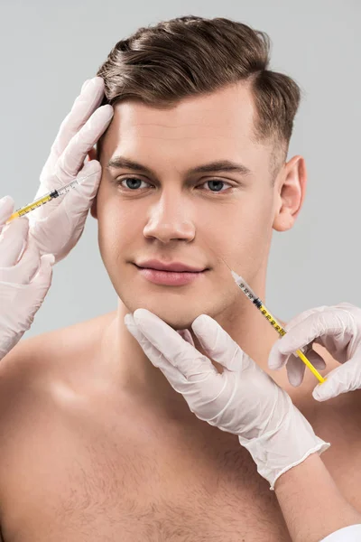Обрезанный вид косметологов в латексных перчатках, делающих инъекции красоты, изолированные на сером — стоковое фото