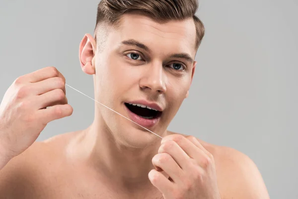 Beau jeune homme nettoyage des dents avec fil dentaire isolé sur gris — Photo de stock