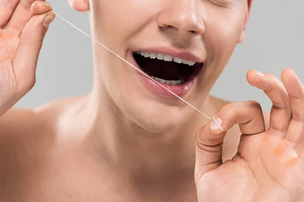Vista recortada del joven limpiando dientes con hilo dental aislado en gris - foto de stock