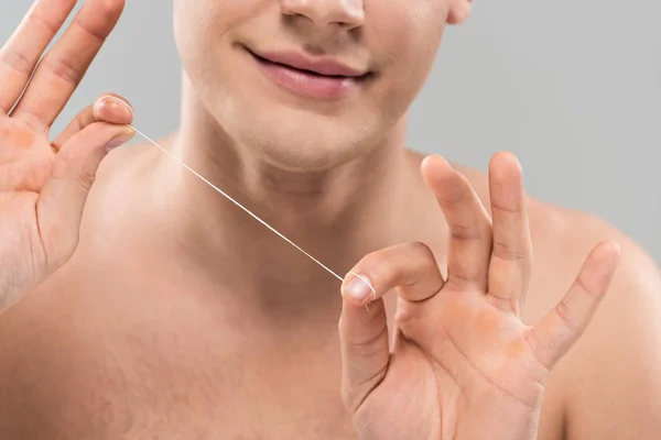 Обрезанный вид обнаженного молодого человека, держащего зубную нить изолированной на сером — стоковое фото