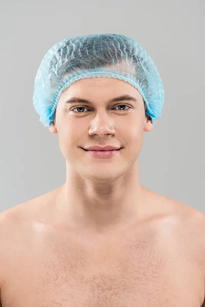 Вид спереду усміхненого голого молодого чоловіка в медичній шапці ізольовано на сірому — стокове фото