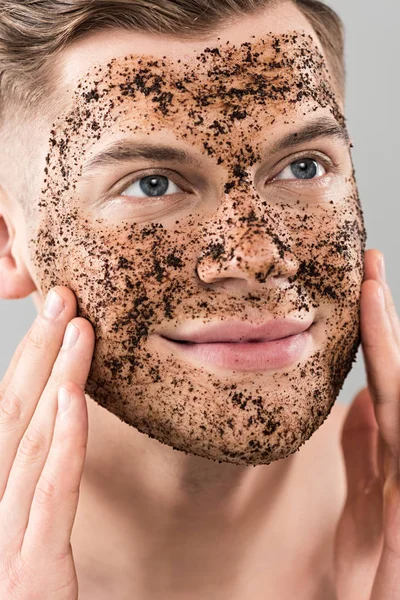 Smiling young man applying scrub isolated on grey — Stock Photo