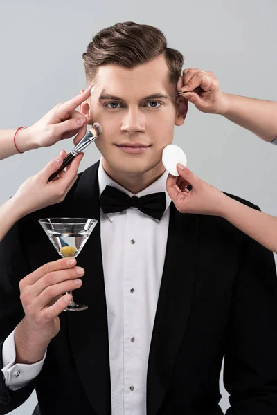 Vue recadrée de maquilleurs faisant du maquillage pour homme en tenue formelle tenant verre de cocktail isolé sur gris — Photo de stock
