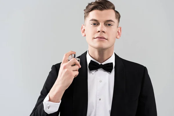 Front view of confident man in formal wear applying perfume isolated on grey — Stock Photo