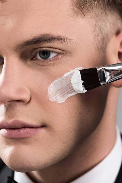 Vista de cerca del hombre aplicando crema en la cara con cepillo cosmético - foto de stock