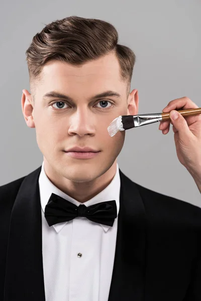 Partial view of cosmetologist applying face cream and man in formal wear isolated on grey — Stock Photo