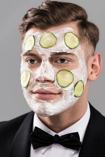Junger Mann in formeller Kleidung mit Gurken-Gesichtsmaske isoliert auf grau — Stock Photo