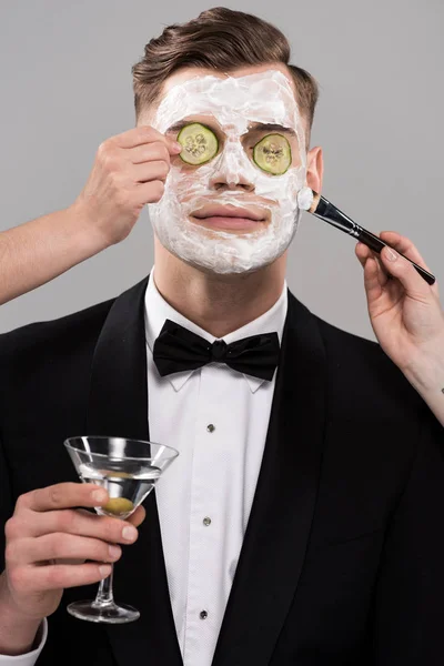 Обрезанный вид косметологов, надевающих огуречную маску и мужчину в формальной одежде, держащих стакан мартини — стоковое фото