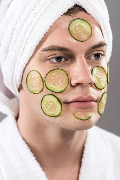 Jovem em roupão de banho com pepinos cortados no rosto isolado em cinza — Fotografia de Stock