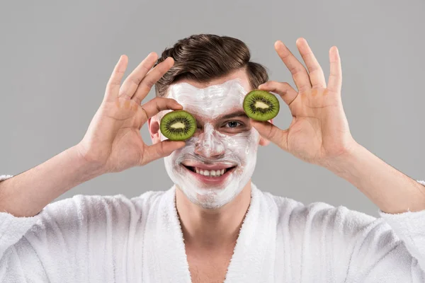 Vue de face de l'homme souriant en peignoir tenant kiwi coupé isolé sur gris — Photo de stock