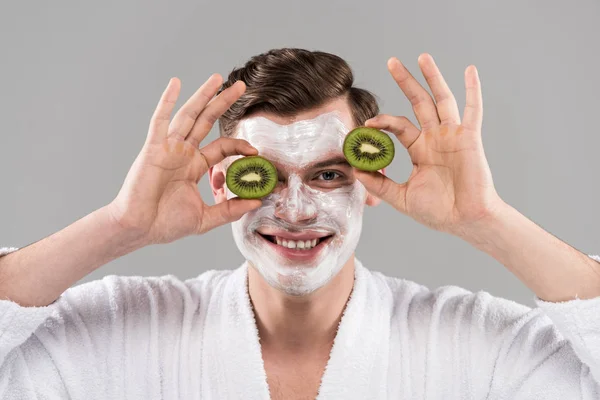 Vista frontal do homem sorridente em roupão segurando kiwi corte isolado em cinza — Fotografia de Stock