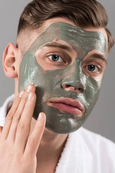 Trauriger junger Mann berührt Tonmaske isoliert auf Grau — Stockfoto