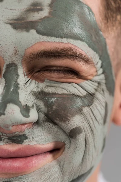 Cropped view of smiling young man with clay mask with closed eye — Stock Photo