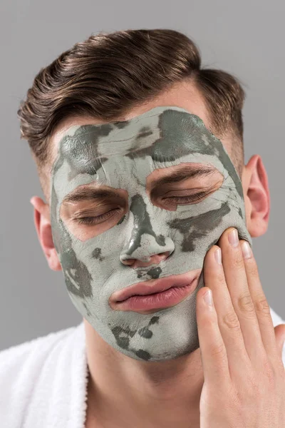 Scontento giovane uomo con maschera di argilla toccare viso isolato su grigio — Foto stock