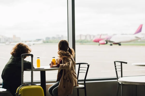 Dos niños sentados en la sala de espera y mirando por la ventana en el avión - foto de stock