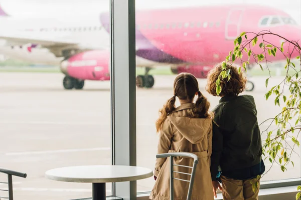 Two kids standing near table and plant and looking on plane — Stock Photo