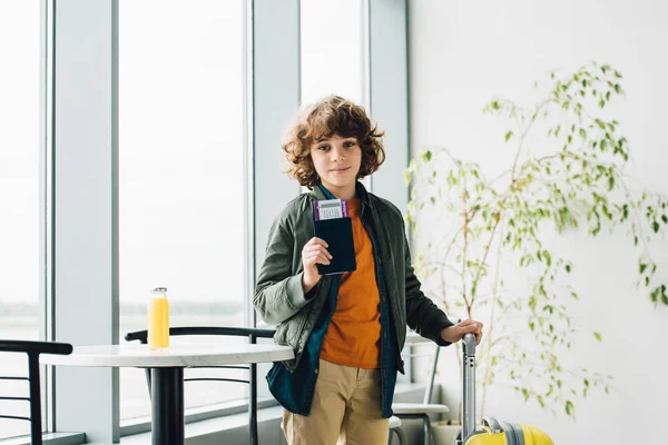 Boy standing with yellow suitcase, holding passport and ticket in airport — Stock Photo