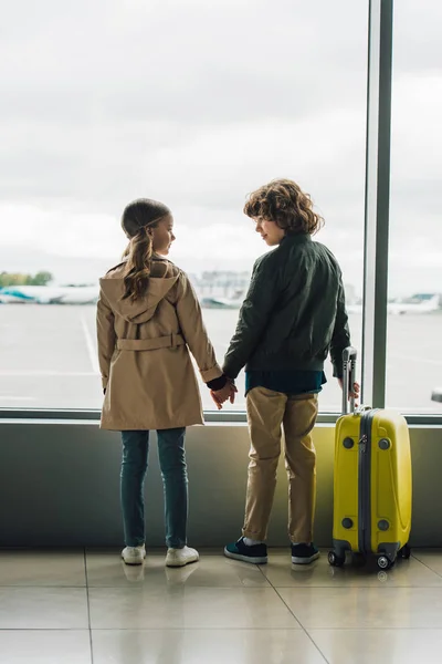 Back view of kids holding hands and looking at each other near window in airport — Stock Photo