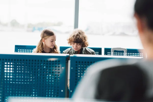 Дети сидят и разговаривают в зале ожидания с синими сиденьями в аэропорту — стоковое фото