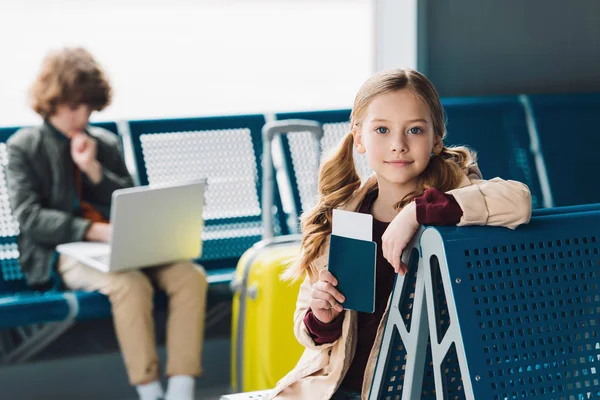 Selective focus on preteen kid holding passport and sitting on blue seat in waiting hall — Stock Photo