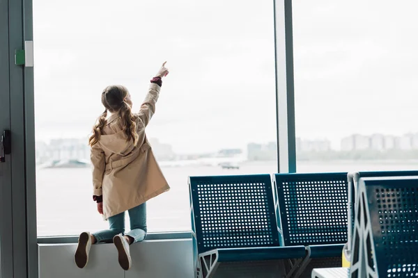 Back view of preteen kid pointing with finger at window in airport — Stock Photo