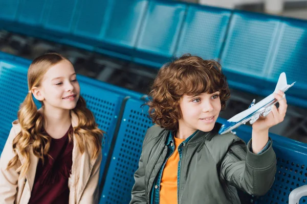 Cute preteen kids sitting in waiting hall and playing with toy plane — Stock Photo