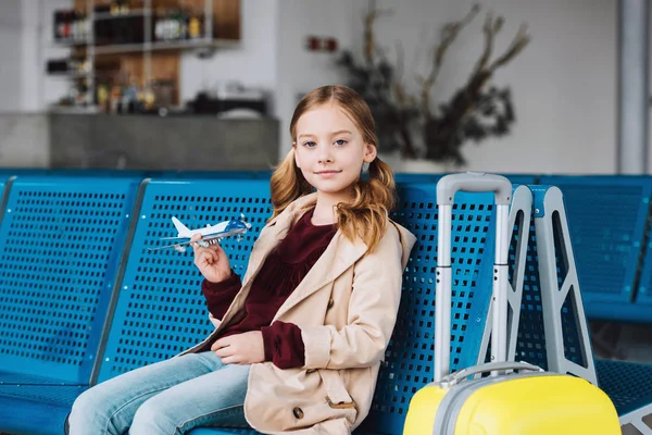 Preteen kid holding toy plane in airport departure lounge and looking at camera — Stock Photo
