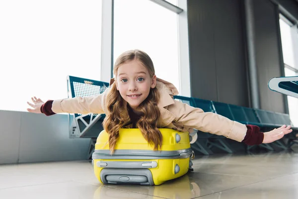 Niño preadolescente emocionado acostado en la maleta con las manos extendidas en la sala de salida del aeropuerto - foto de stock