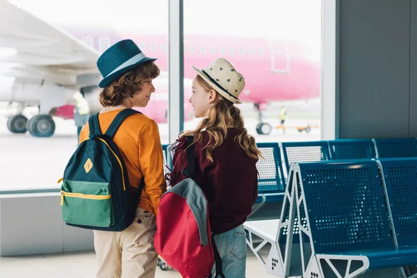 Vista trasera de los niños preadolescentes con mochilas en la sala de espera mirándose entre sí - foto de stock