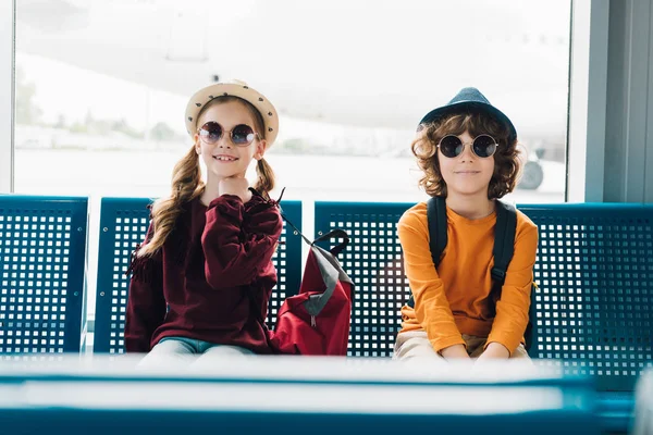 Cute preteen kids in sunglasses sitting in waiting hall — Stock Photo