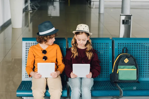 Cute preteen kids sitting in waiting hall and using Digital Tablets — Stock Photo