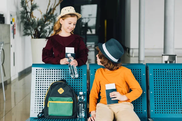 Cute preteen kids in waiting hall with air tickets and passports looking at each other — Stock Photo