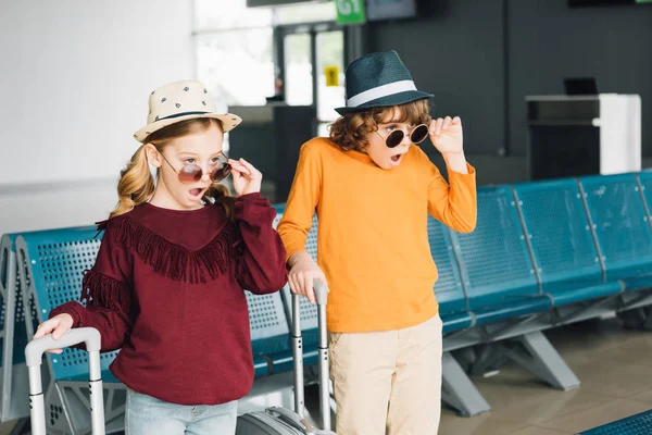 Impactados niños preadolescentes en gafas de sol con maletas en la sala de espera - foto de stock