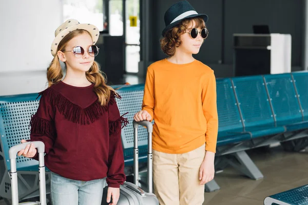 Niños preadolescentes en gafas de sol con maletas en la sala de espera - foto de stock