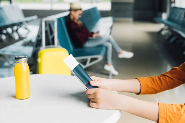 Vue recadrée du préadolescent tenant un passeport et un billet d'avion à l'aéroport sur la table avec du jus d'orange — Photo de stock