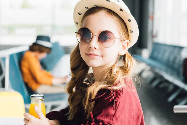 Niedliche preteen Kind mit Sonnenbrille sitzt mit Orangensaft in Wartehalle — Stockfoto